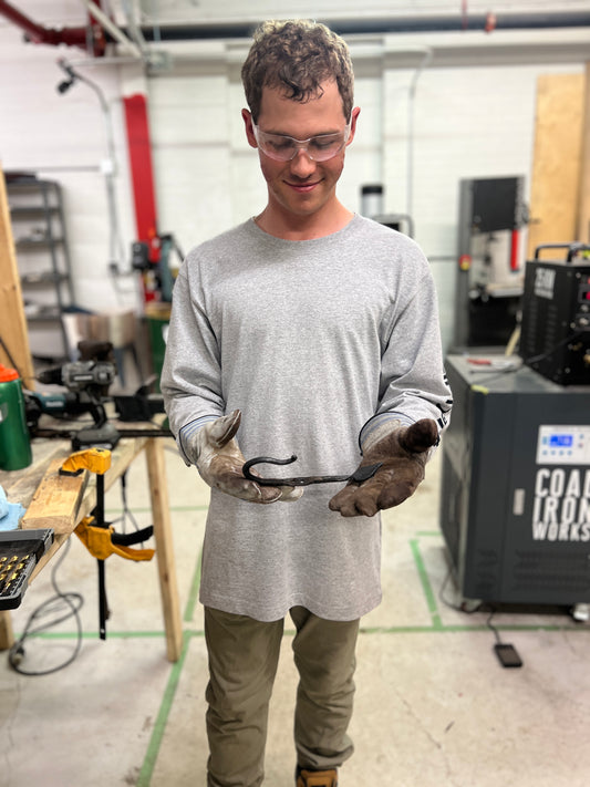 Participant in Toronto blacksmithing workshop at Oldboy Metal Co. holding hand-forged wall hook made during beginner forging class
