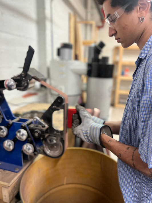 Beginner blacksmith using a belt grinder to shape metal during a workshop at Oldboy Metal Co in Toronto.