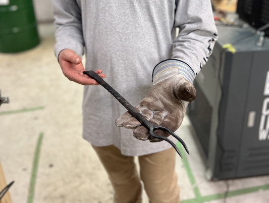 Student holding a hand-forged blacksmithing fork made during a beginner workshop at Oldboy Metal Co in Toronto.