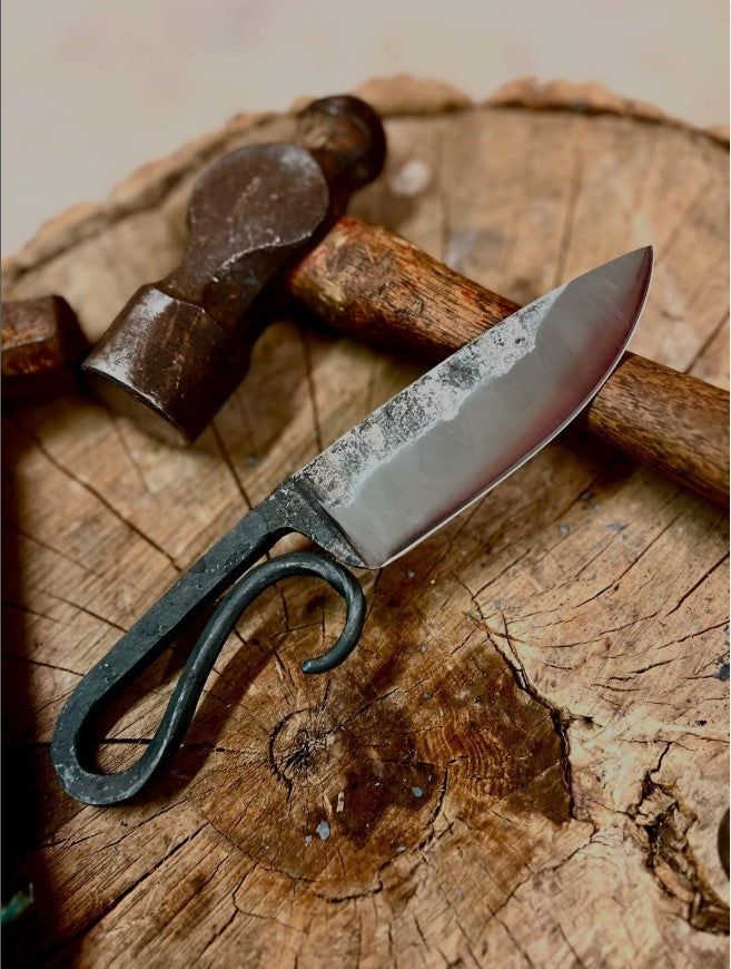 Toronto blacksmith-forged knife with twisted handle and hammer on rustic wooden background, made in one-day knife making workshop